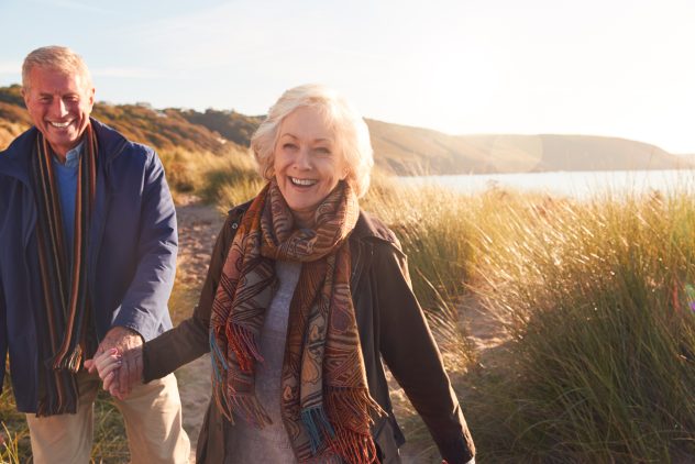 Loving Active Senior Couple Holding Hands As They Walk Through Sand Dunes