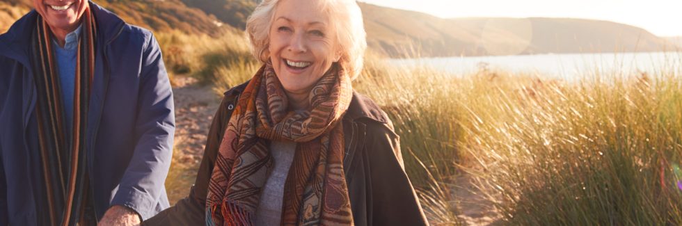 Loving Active Senior Couple Holding Hands As They Walk Through Sand Dunes