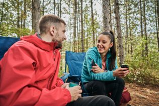 Cheerful camping couple enjoying talking and tea in the forest