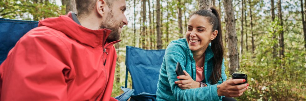 Cheerful camping couple enjoying talking and tea in the forest