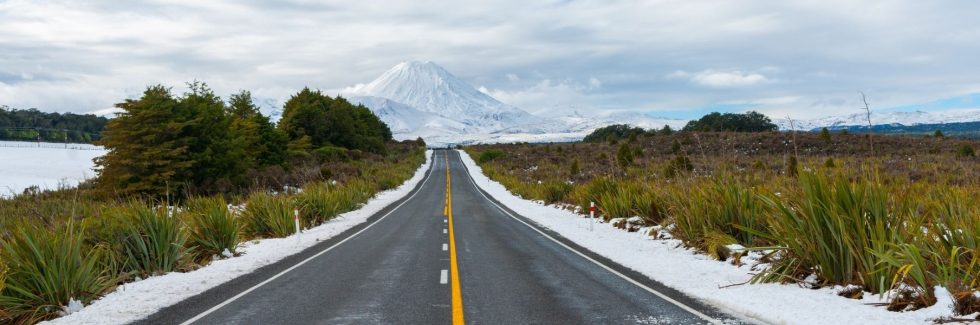 Long road through snowy landscape leading to snow-capped Mount Ngauruhoe in New Zealand