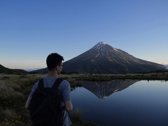 man standing in front on a lake with mt taranaki in background.