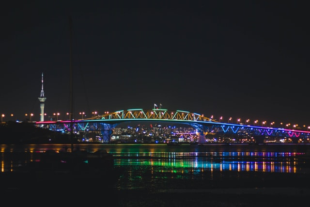 coloured lights on auckland harbour bridge with city in background